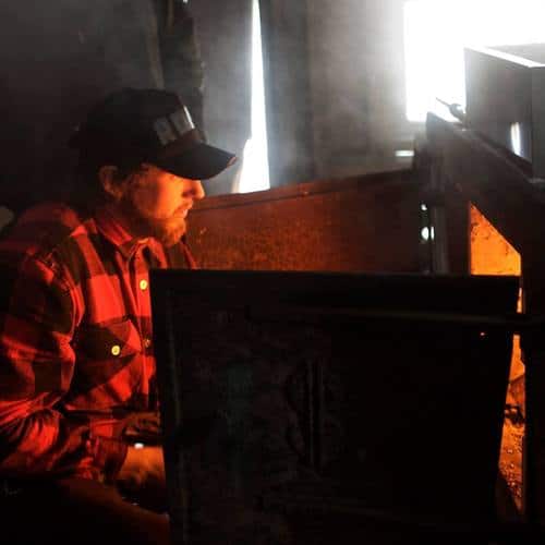 A Man looks into a wood burning fire.